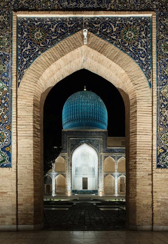 A brick archway framing the turquoise dome of a Timurid monument in Samarkand