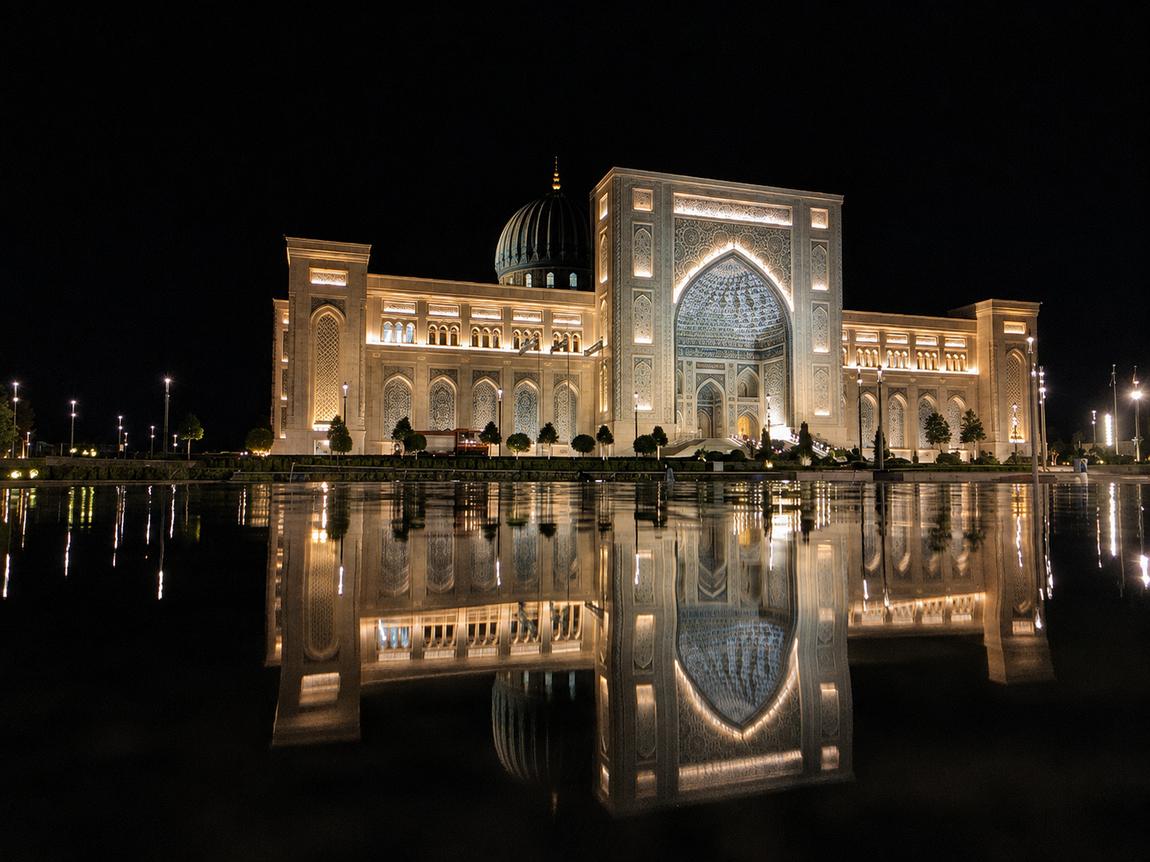 A floodlit monumental portal and dome in Tashkent mirrored in a still pool at night