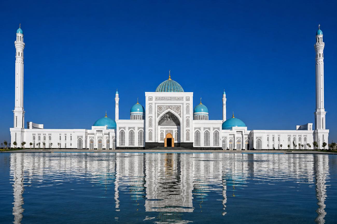 A white marble mosque with turquoise domes and minarets mirrored in a still reflecting pool